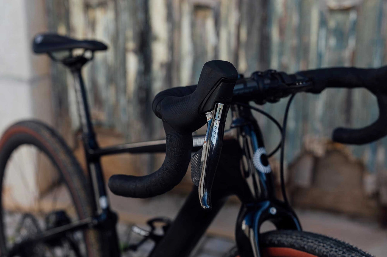 Close-up view of bicycle handlebars and shifters against a blurred rustic background.