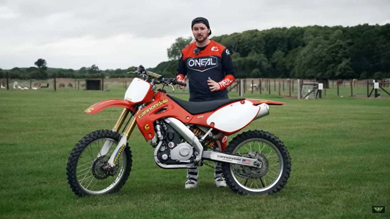 Person standing next to a red Cannondale motocross bike in a grassy field.