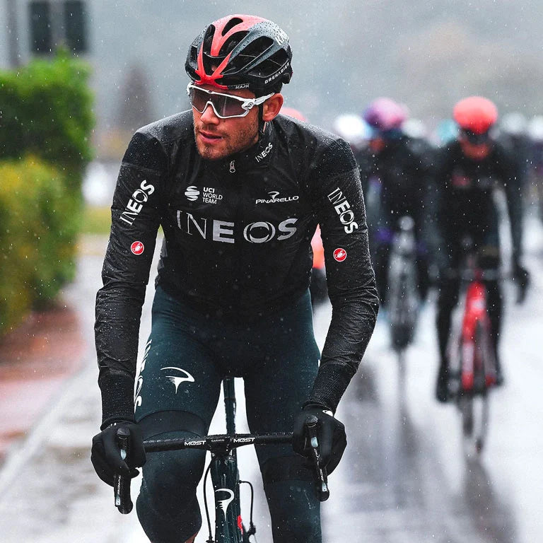 Cyclist wearing INEOS gear riding a bicycle in rainy weather.