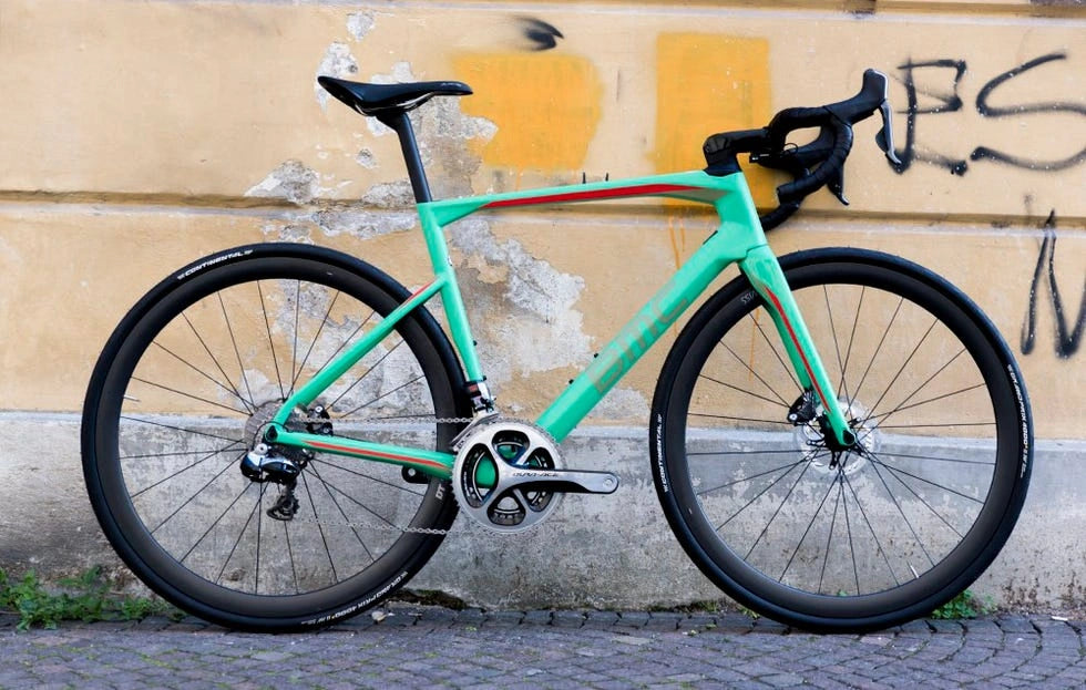 A green road bicycle with black tires leaning against a yellow wall with graffiti.