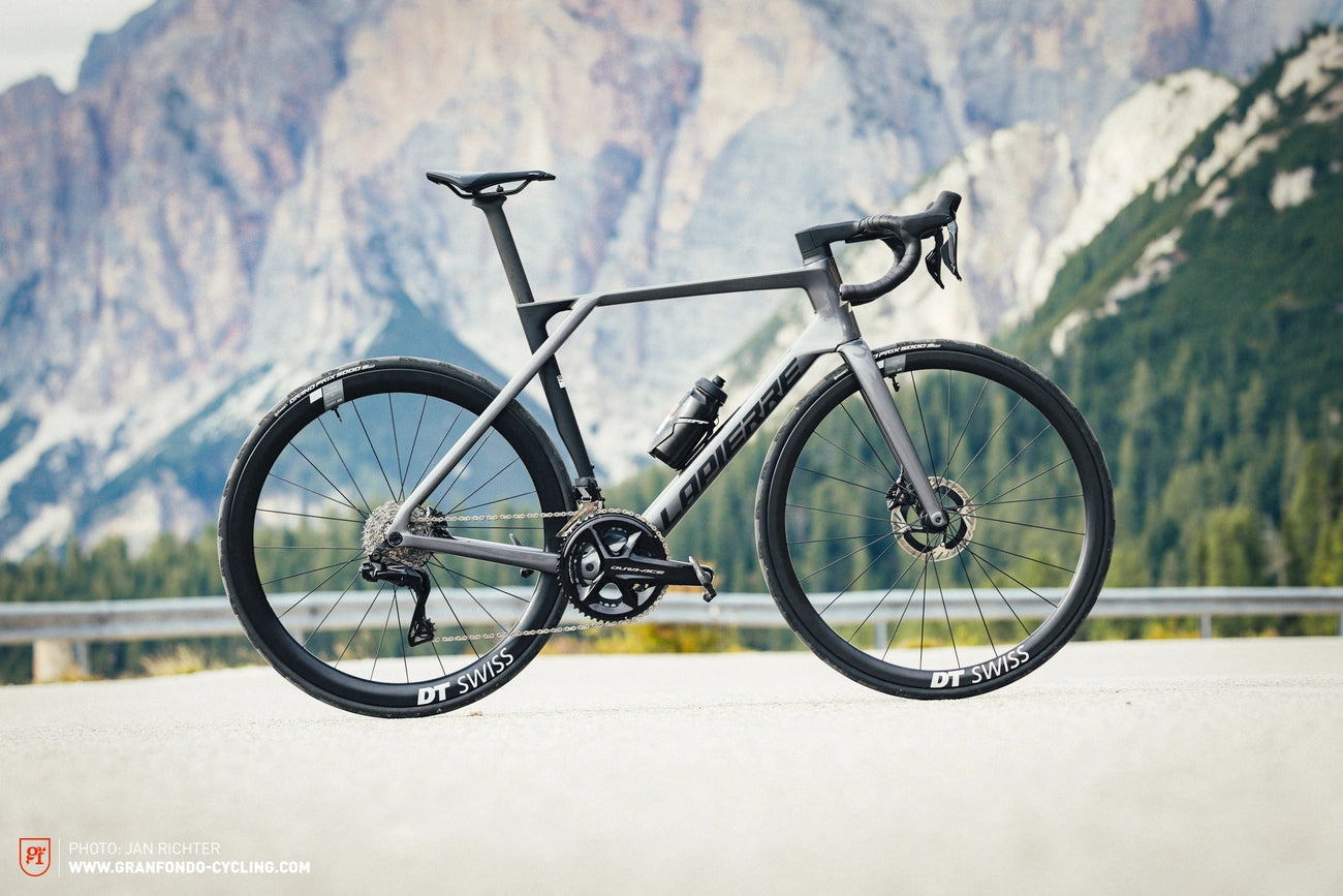 A modern road bike standing on a pavement with a backdrop of majestic mountains.