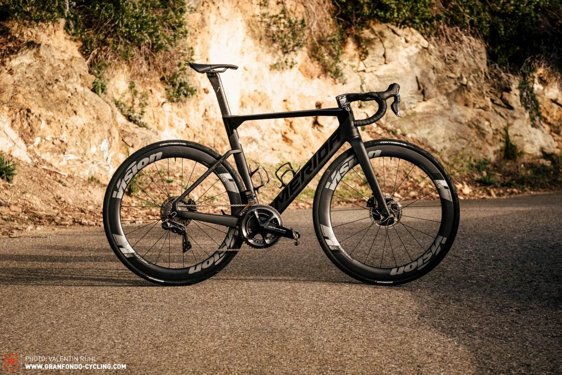 A modern road bike with a sleek black frame and aerodynamic design parked on a scenic roadside.