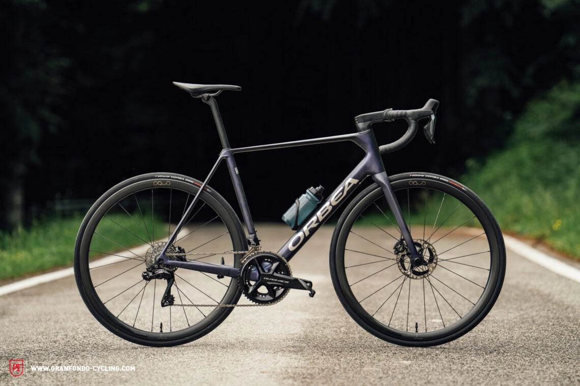 A sleek Orbea road bike with a water bottle on a forest road.