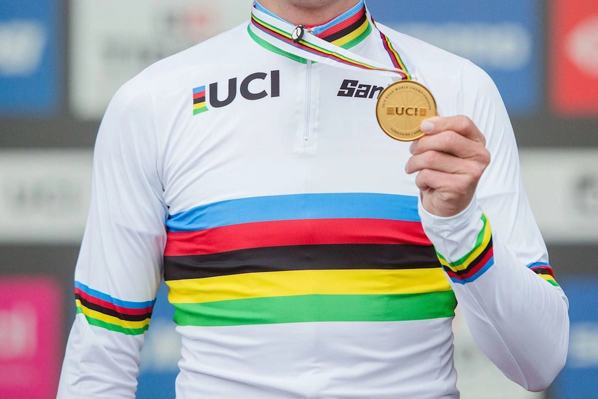 Cyclist holding a UCI World Champion medal wearing a rainbow-striped jersey.